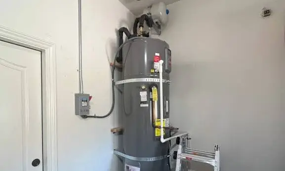 Heat pump water heater installed in a closet, showing the compressor and condensate line at the top of the unit